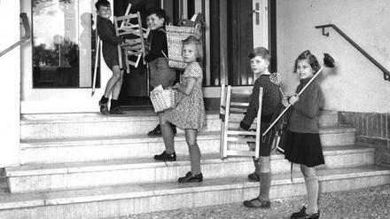 Fünf Kinder tragen Stühle und anderes ins Nachbarschaftsheim Berlin-Neukölln in den Fünfzigerjahren.
