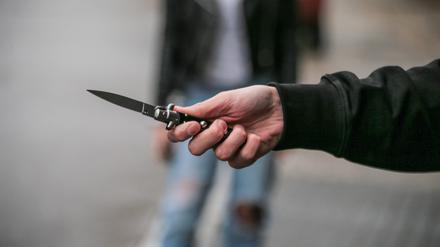 Männerhand mit einem verbotenen Springmesser auf der Straße.