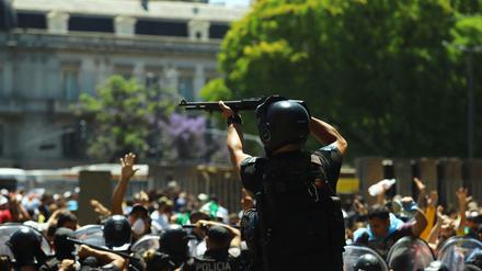 Ein Polizist hält eine Waffe hoch, als Menschen während der Totenwache für Diego Maradona mit der Polizei zusammenstoßen.