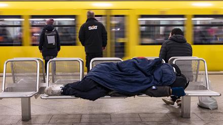 Ein Obdachloser schläft auf einer Bank am Bahnhof Alexanderplatz in Berlin-