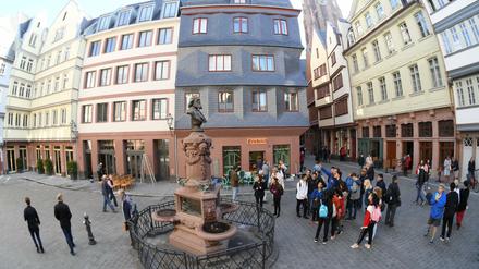 Touristen stehen auf dem Hühnermarkt der neuen Frankfurter Altstadt am restaurierten Friedrich-Stoltze-Brunnen.