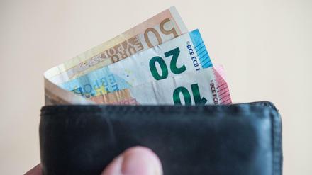Geldscheine im Wert von fünf, zehn, zwanzig, fünfzig und hundert Euro stecken in einem Geldbeutel, der von einer Hand gehalten wird.