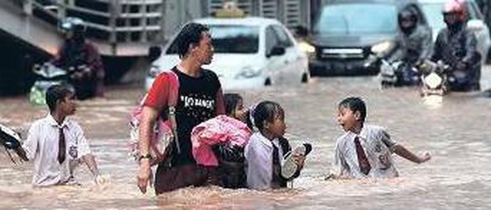 Schulkinder überqueren völlig durchnässt eine Straße im Banken- und Geschäftsviertel der Stadt. Sieben von zehn Bezirken sind überflutet. 