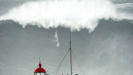 Monsterwelle. Etwa 30 Meter hoch ist diese Welle vor Nazaré in Portugal, auf der ein winziger Surfer zu sehen ist. 