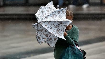 Eine junge Frauen kämpft in Berlin bei Starkwind mit einem Regenschirm. (Symbolbild)