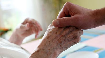 Ein Pfleger hält die Hand der Bewohnerin eines Pflegeheimes.