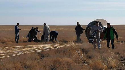 Rettungsmannschaften stehen neben der notgelandeten russischen Sojus-Kapsel in der Steppe von Kasachstan.