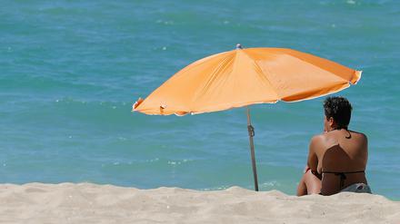 Eine Frau sitzt am Strand von Arenal auf Mallorca unter einem Sonnenschirm.