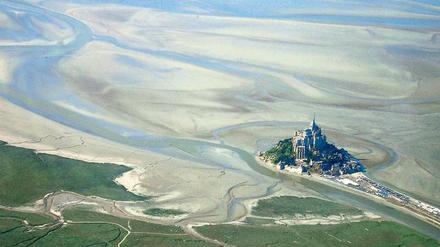 Land in Sicht. Die Vogelperspektive lässt erahnen, welch’ Schicksal Mont Saint-Michel vor der Küste der Normandie droht, weil die Natur außer Kraft gesetzt wurde.