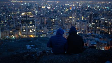 Zwei junge Männer sitzen nach Sonnenuntergang über den Dächern der Millionenmetropole Teheran.  