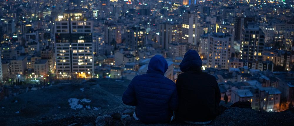Zwei junge Männer sitzen nach Sonnenuntergang über den Dächern der Millionenmetropole Teheran.  