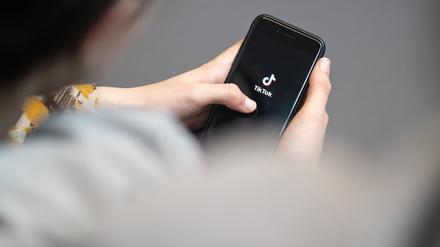 Eine Jugendliche schaut auf ein Smartphone mit angezeigtem TikTok Logo. Auf der Online-Plattform gibt es vermehrt extremistische Influencer, die Jugendliche gezielt ködern wollen.