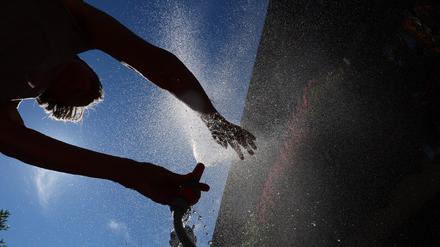 15.07.2023, Bayern, Kaufbeuren: Eine Frau kühlt sich in einem Garten mit Wasser aus einem Gartenschlauch ab.