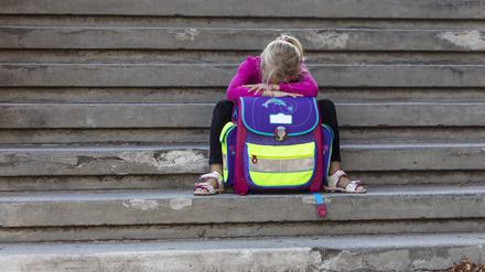 Ein Mädchen sitzt mit Schultasche auf einer Treppe.