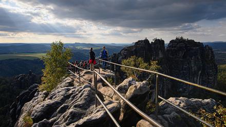 Wanderer blicken von der Schrammsteinaussicht in der Sächsischen Schweiz auf die Felsen der Schrammsteine. 