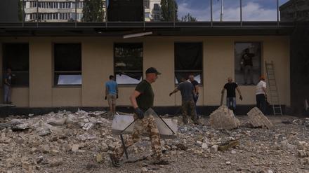 Menschen räumen nach russischen Drohnenangriffen Trümmer vor einem beschädigten Regierungsgebäude weg.