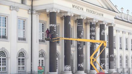 Der Künstler Dan Perjovschi malt im Rahmen der Documenta 15 Slogans auf die Säulen vor dem Fridericianum. 