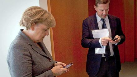 Bundeskanzlerin Angela Merkel und Regierungssprecher Steffen Seibert mit ihren Smartphones.