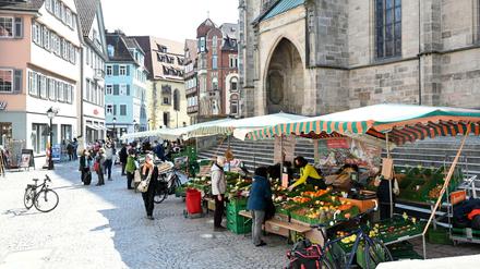 Passanten gehen in der Fußgängerzone in Tübingen an Marktständen vorbei.