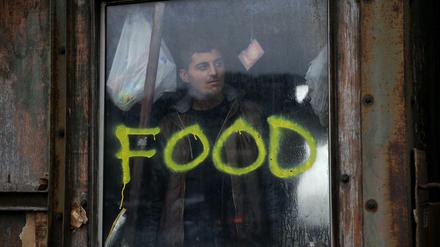 Ein Flüchtling steht an einem Fenster mit der Aufschrift "Food" in einer verlassenen Lagerhalle, die einigen Hunderten Flüchtlingen Schutz bietet, in Belgrad.
