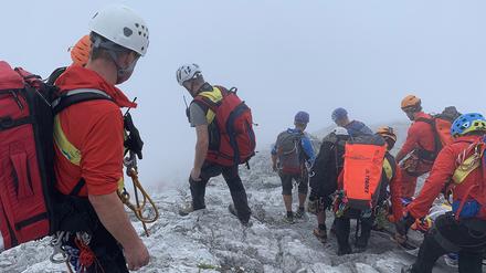 Bergretter transportieren in dichtem Nebel eine zuvor am Watzmann abgestürzte Bergsteigerin auf einer Trage den Berg hinunter. 