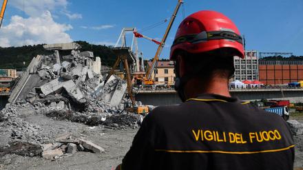 Ein Feuerwehrmann schaut auf Bagger, die Trümmer der teilweise eingestürzten Morandi-Autobahnbrücke entfernen.
