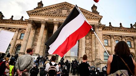 Teilnehmer einer Kundgebung gegen die Corona-Maßnahmen stehen vor dem Reichstag, ein Teilnehmer hält eine Reichsflagge.