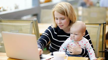 Eine junge Mutter sitzt mit ihrem Baby auf dem Schoß vor einem Laptop. (Symbolbild)