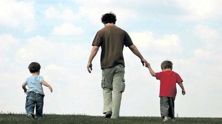Ein Vater läuft mit seinen zwei kleinen Kindern über eine grüne Wiese.