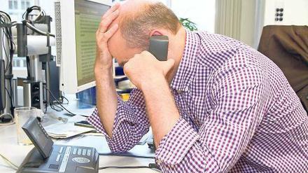 Ein Mann am Arbeitsplatz fasst sich verzweifelt an den Kopf und spricht ins Telefon
