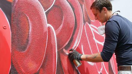 Graffiti-Künstler sprüht rot auf Wand.