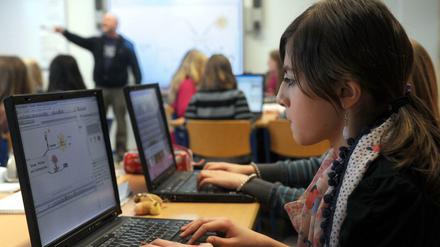 Schülerinnen arbeiten an ihren Laptops, der Lehrer erklärt etwas am Smartboard.