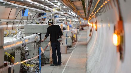 Ein Techniker mit Schutzhelm inspiziert ein aluminiumummanteltes Rohr in einem Tunnel des Teilchenbeschleunigers