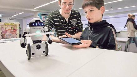 Ein Bibliotheksmitarbeiter erklärt einem Jungen Besucher die Fernsteuerung eines Miniroboters mittels Tablet.