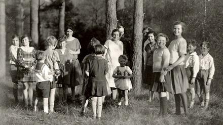 Eine Gruppe Kinder steht mit Erzieherinnen in einem Waldstück.