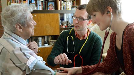 Ein Arzt und eine Medizinstudentin im Gespräch mit einer älteren Patientin in deren Wohnzimmer.