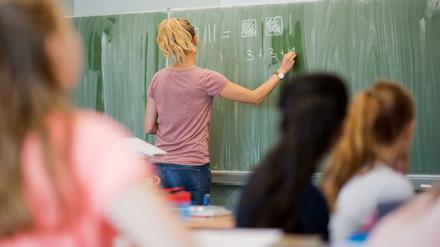 Eine Lehrerin steht vor der Klasse und schreibt eine einfache Gleichung an die Tafel.