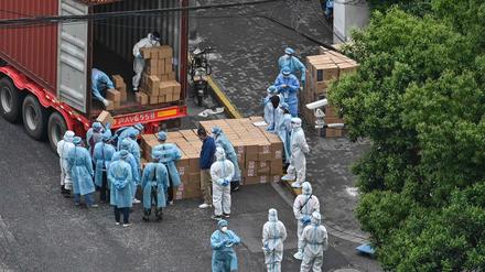 In Shanghai laden Arbeiter in Schutzkleidung einen Truck mit Warenlieferungen aus. 